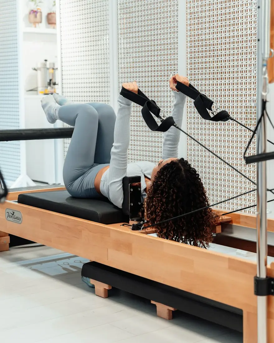 A woman on a reformer presses both legs up into the straps.