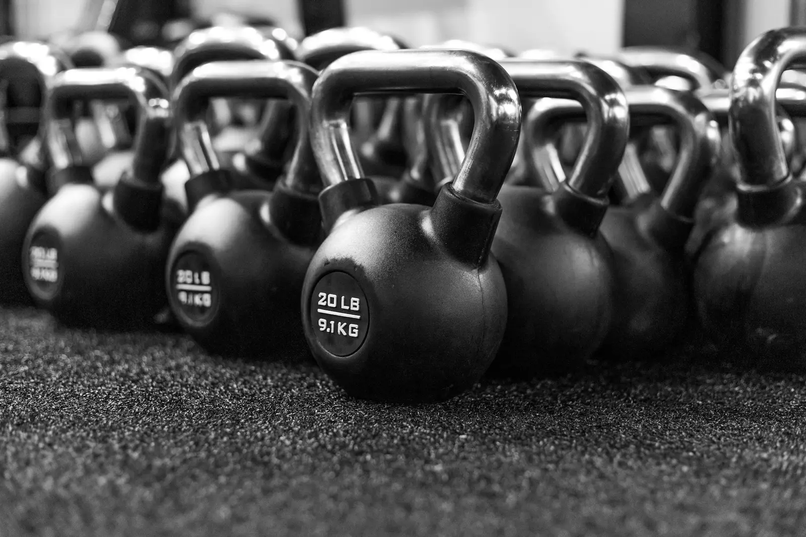 A row of black kettlebells on a rubber gym floor.