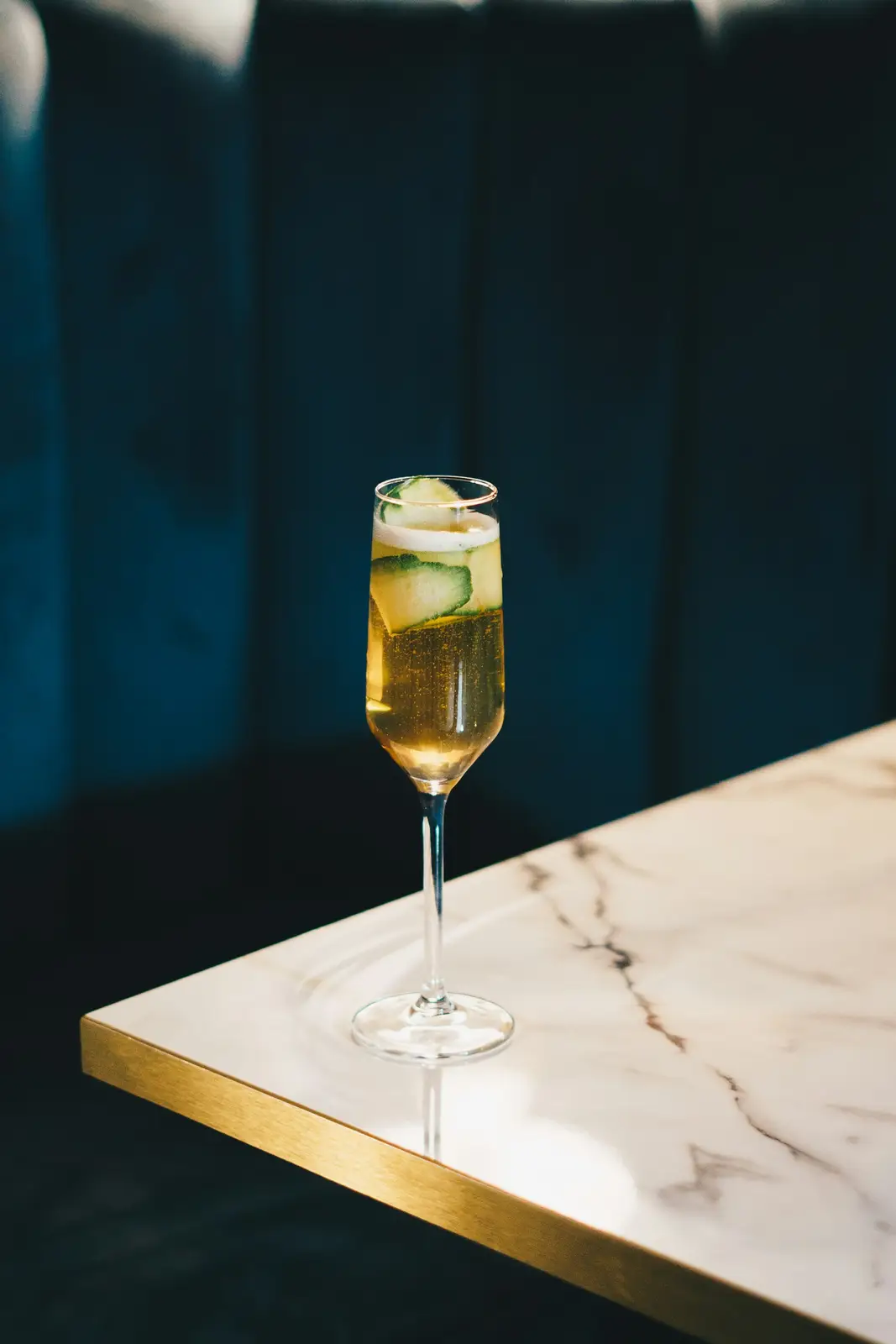 A glass of sparkling wine on a marble bar top against a dark teal wall