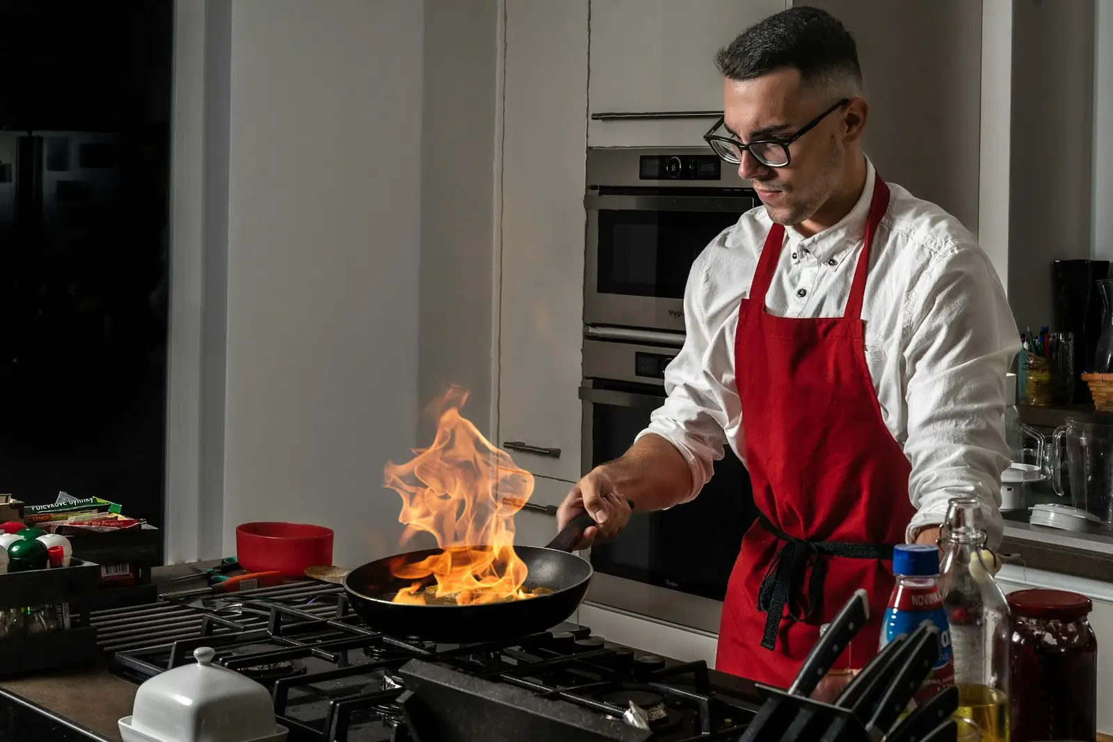 A chef in a red apron flames a pan on the stove