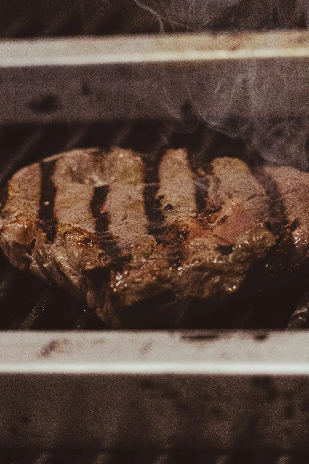 A thick steak searing on a grill with smoke rising