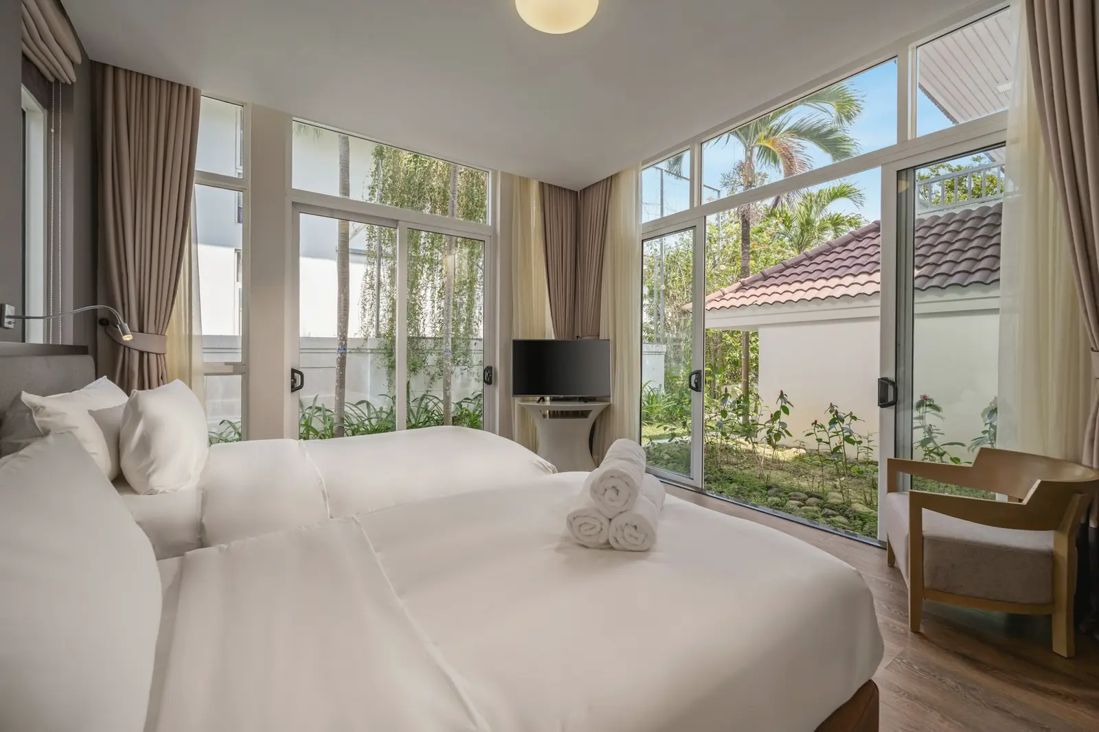 A bright bedroom with white linen, tall windows and palms in the garden beyond