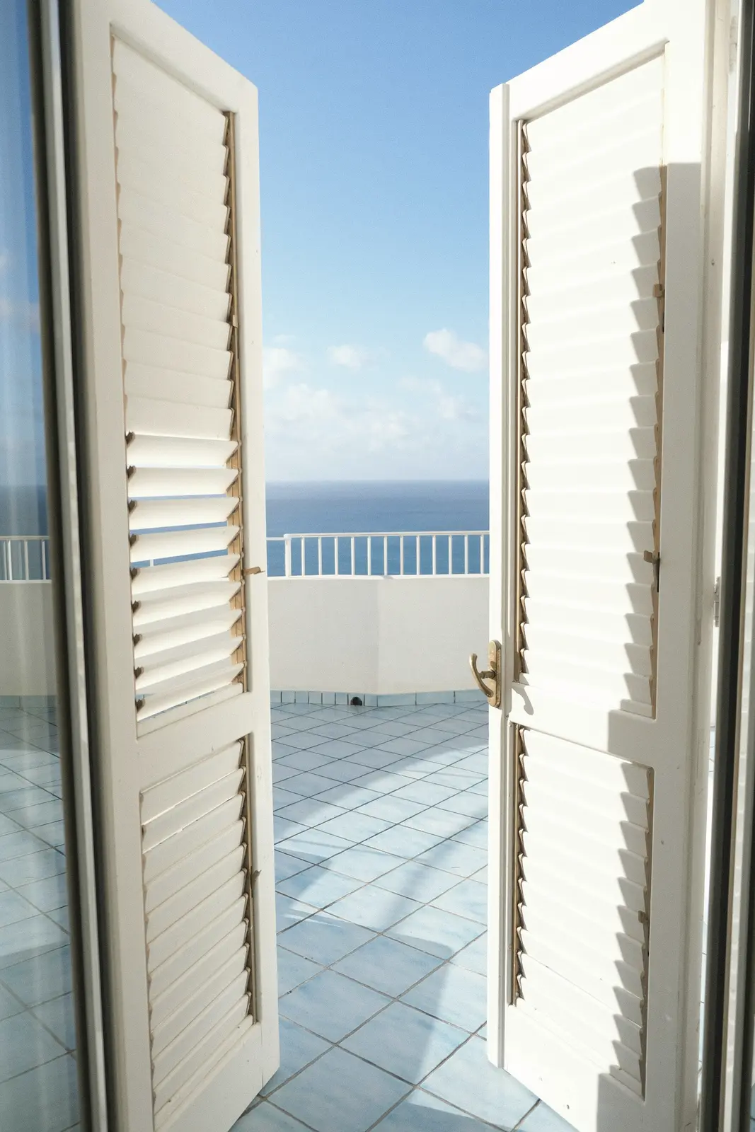 White louvred shutters open onto a tiled balcony and the sea