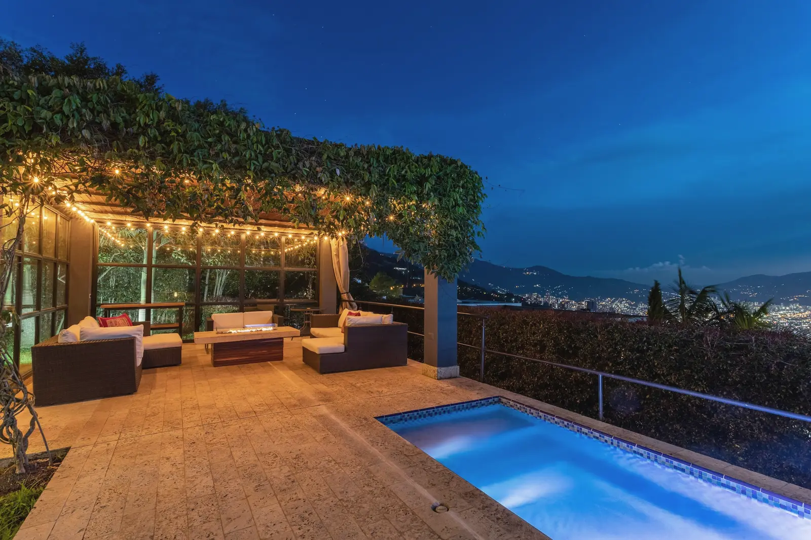 A vine-covered terrace at dusk with a lit plunge pool and the coast below