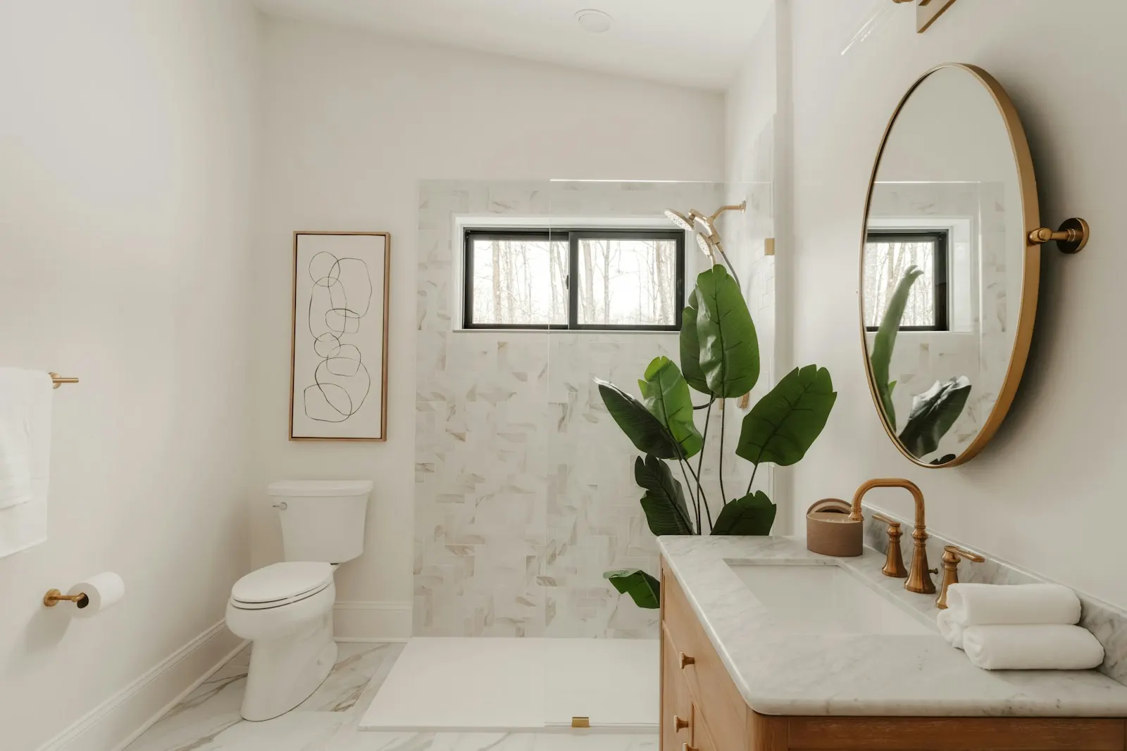 A sunlit bathroom with a marble shower wall, round mirror and wood vanity