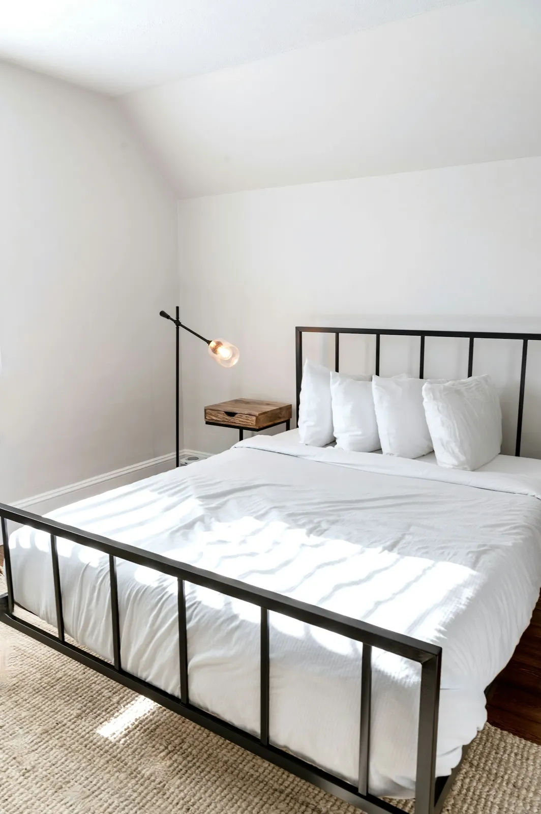 A guest room with a black iron bed made up in crisp white sheets beside a window