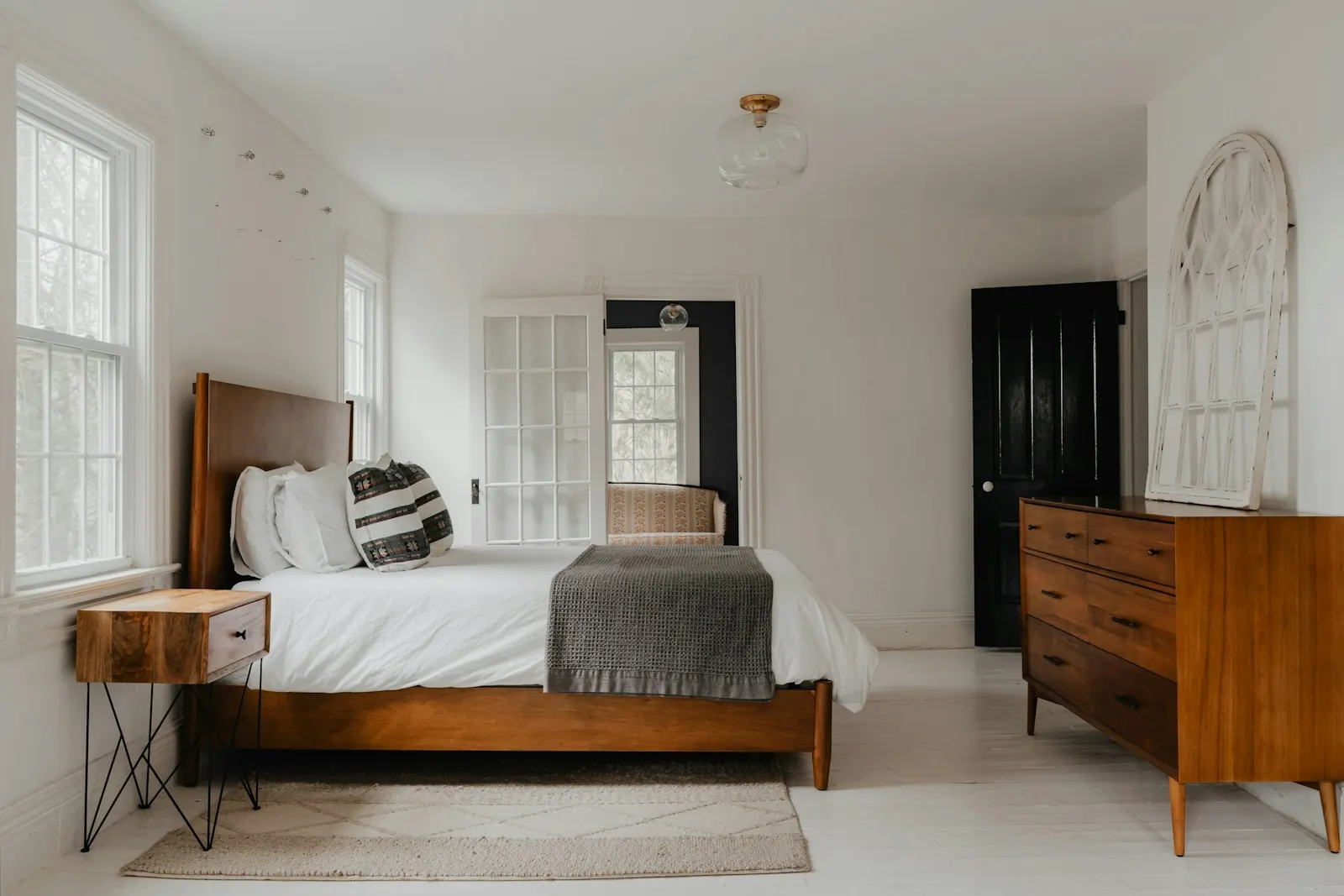 A guest bedroom with a freshly made bed, wood side table and dresser