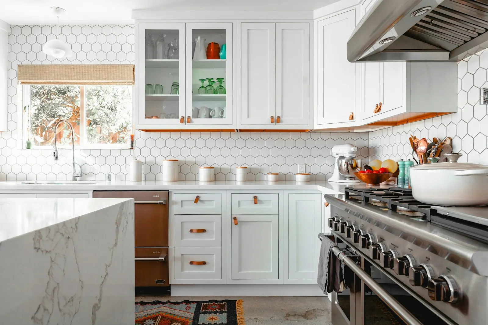 A bright white kitchen with a marble island, hexagon wall tiles and clear counters