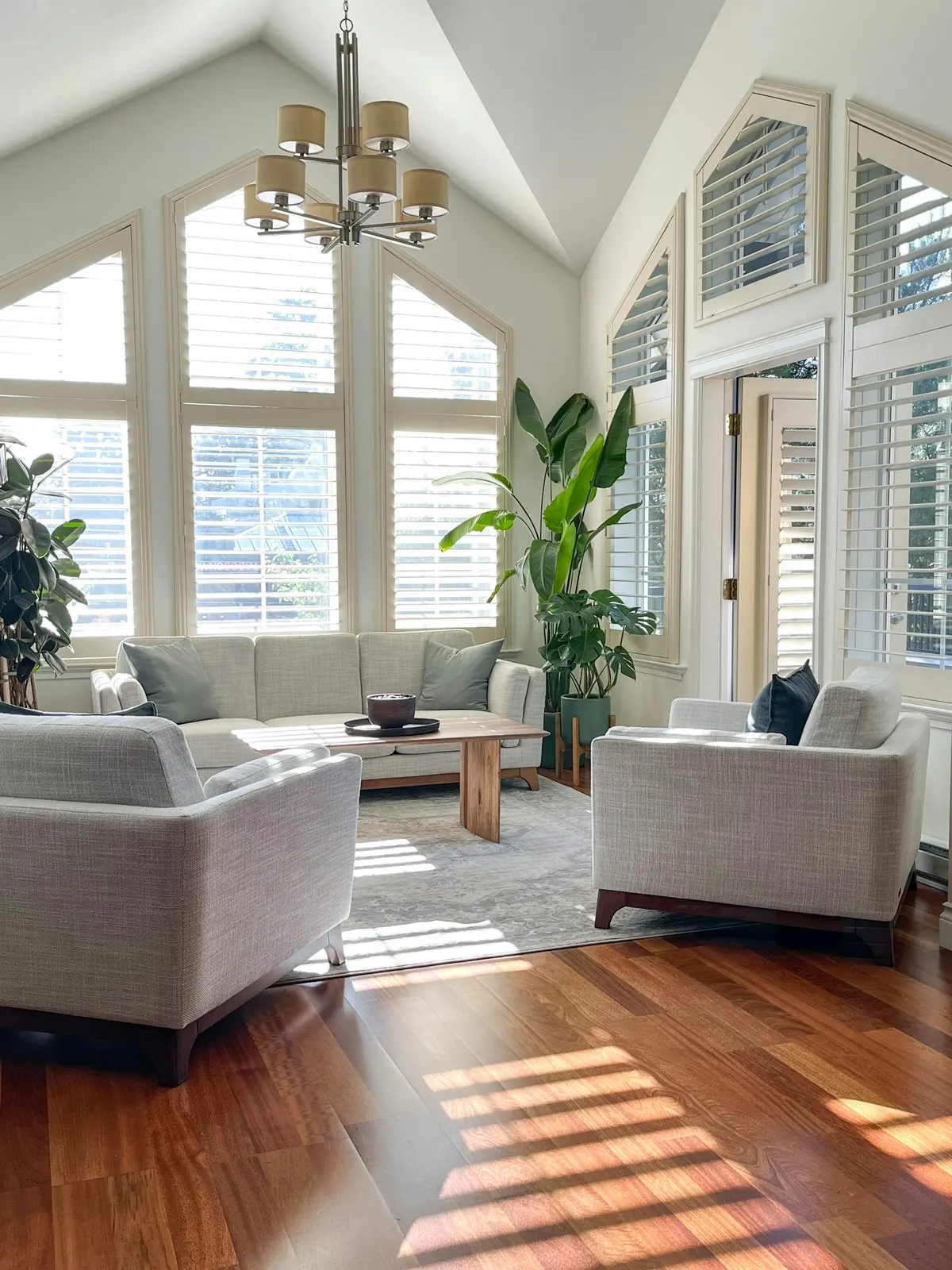 An airy living room with vaulted ceilings, tall windows and light wood floors