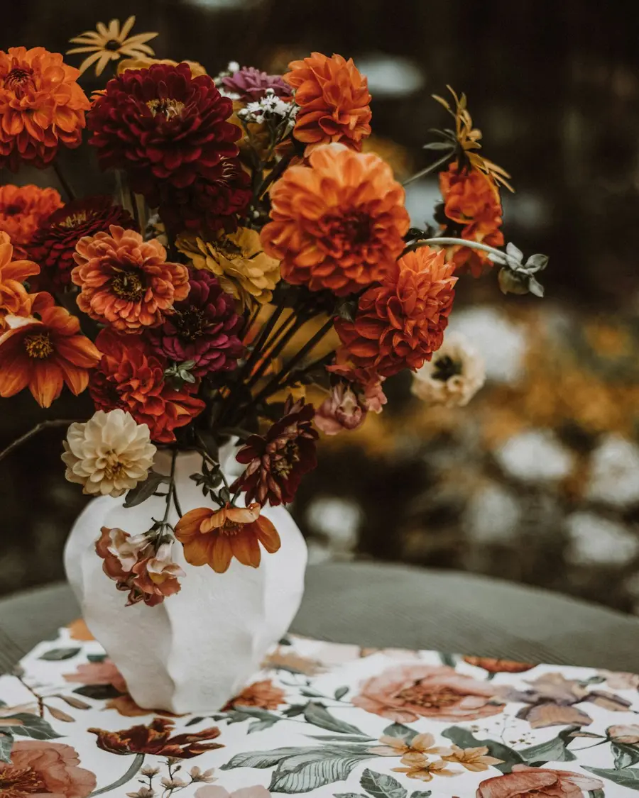 Rust and orange dahlias in a low white vessel on a patterned cloth