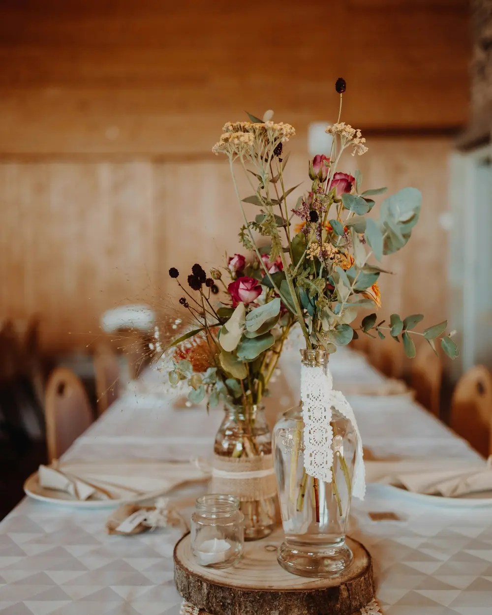 Wildflowers in bottles and a birch round on a long table in a timber barn