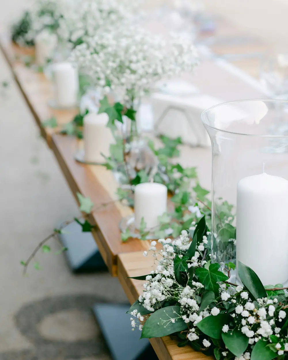 White baby's breath, greenery and pillar candles along a long reception table