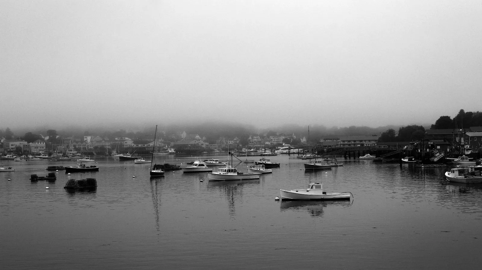 Small boats moored in a still harbour, the town behind them lost in low cloud.