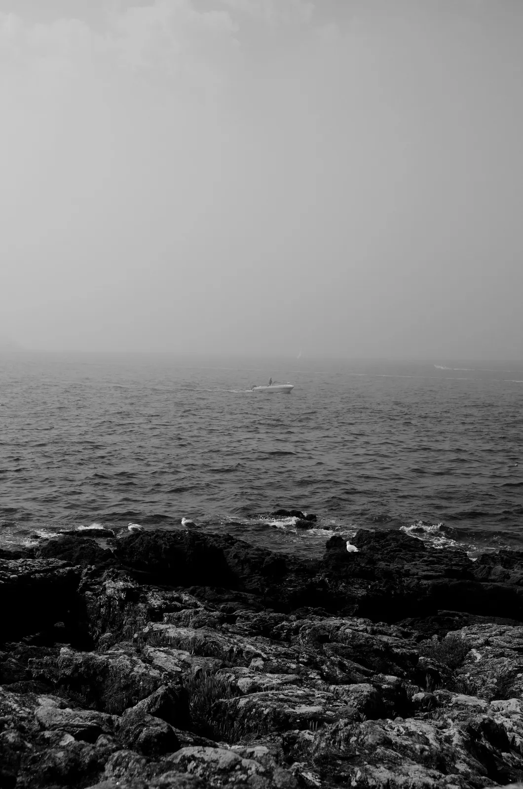 Dark wet rocks in the foreground, a choppy sea beyond and a sky of solid fog.