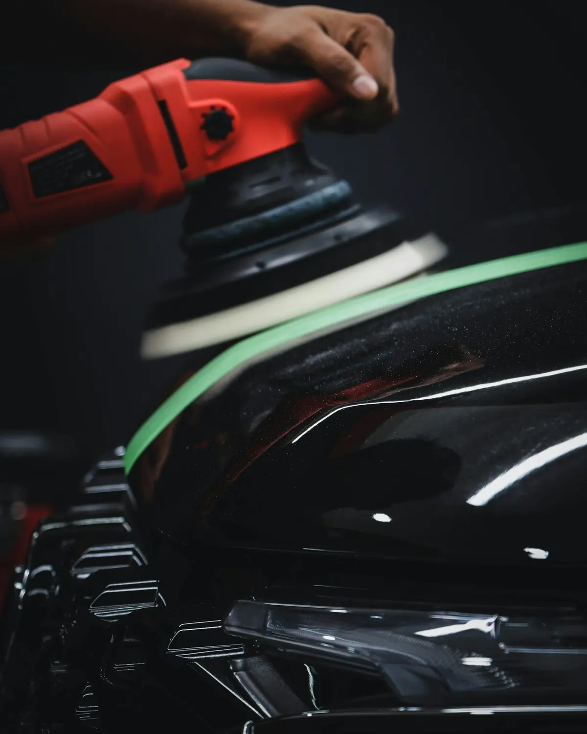 A red dual-action polisher working across glossy black paint