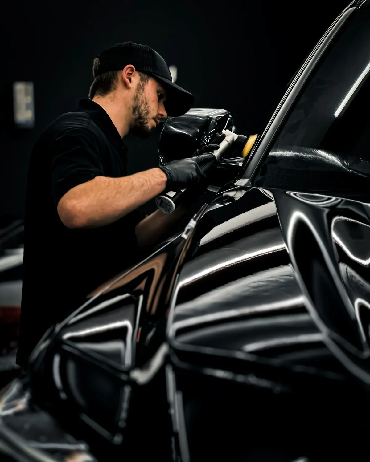 A detailer polishing the front of a black car by hand
