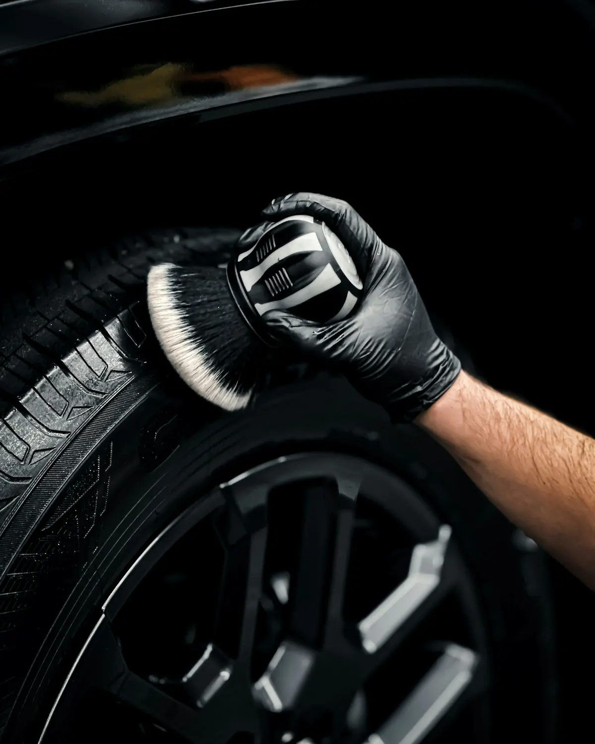 A gloved hand cleaning a tyre sidewall with a soft brush