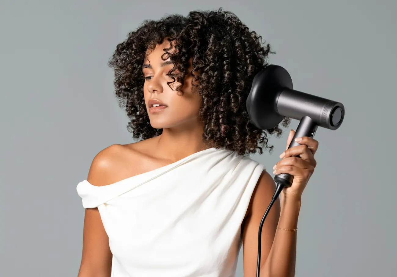 A woman with long defined dark curls holding a hair dryer