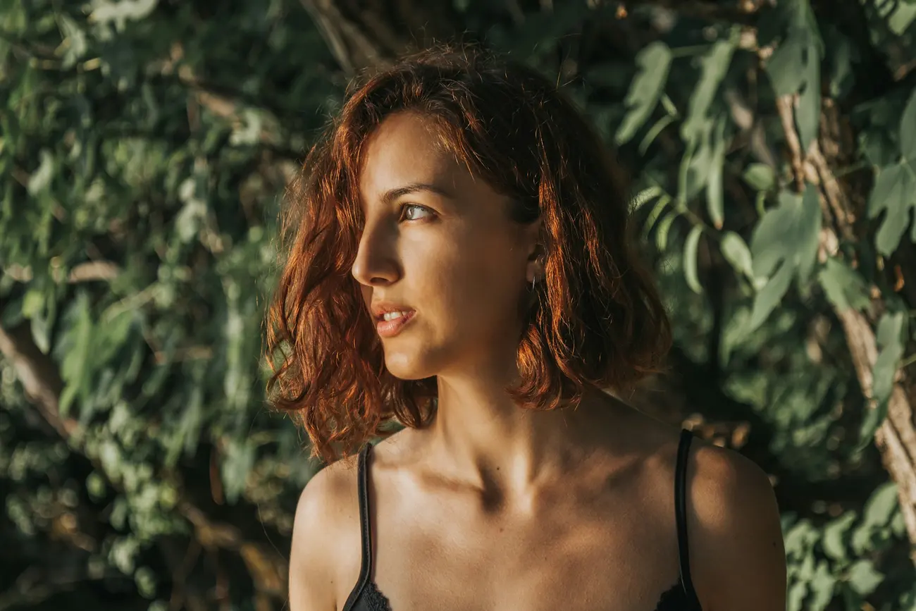 A woman with loose copper-red waves looking to the side in evening light