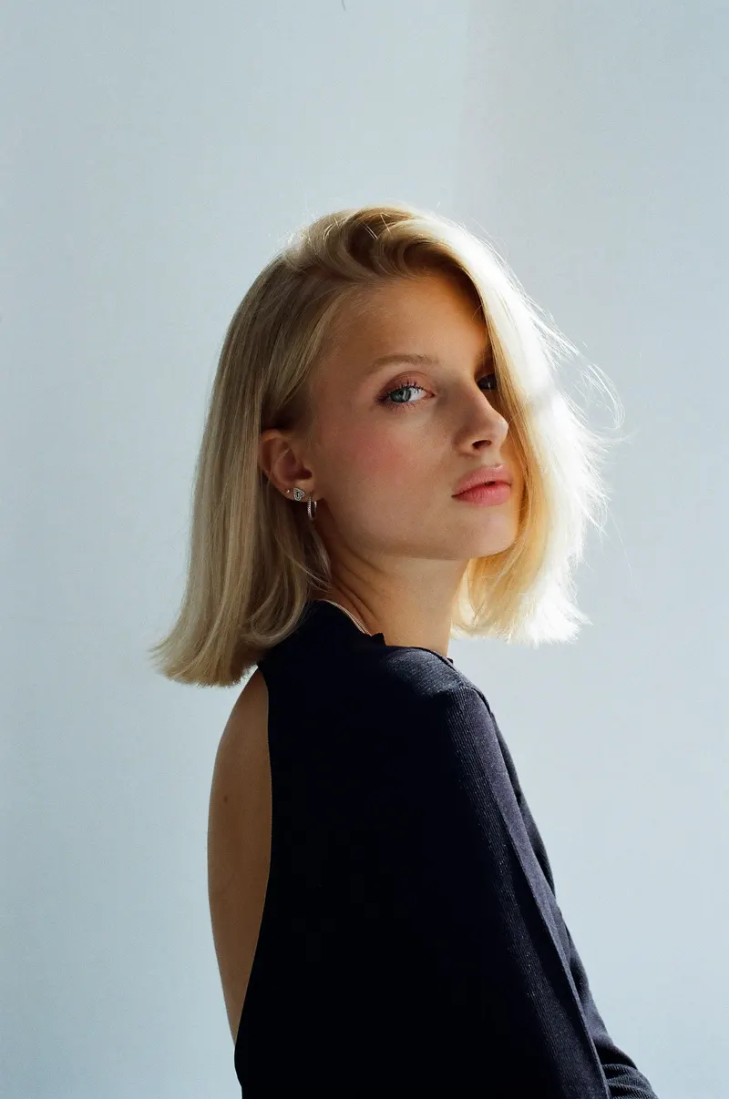 A woman with a blonde lob looking back over her shoulder