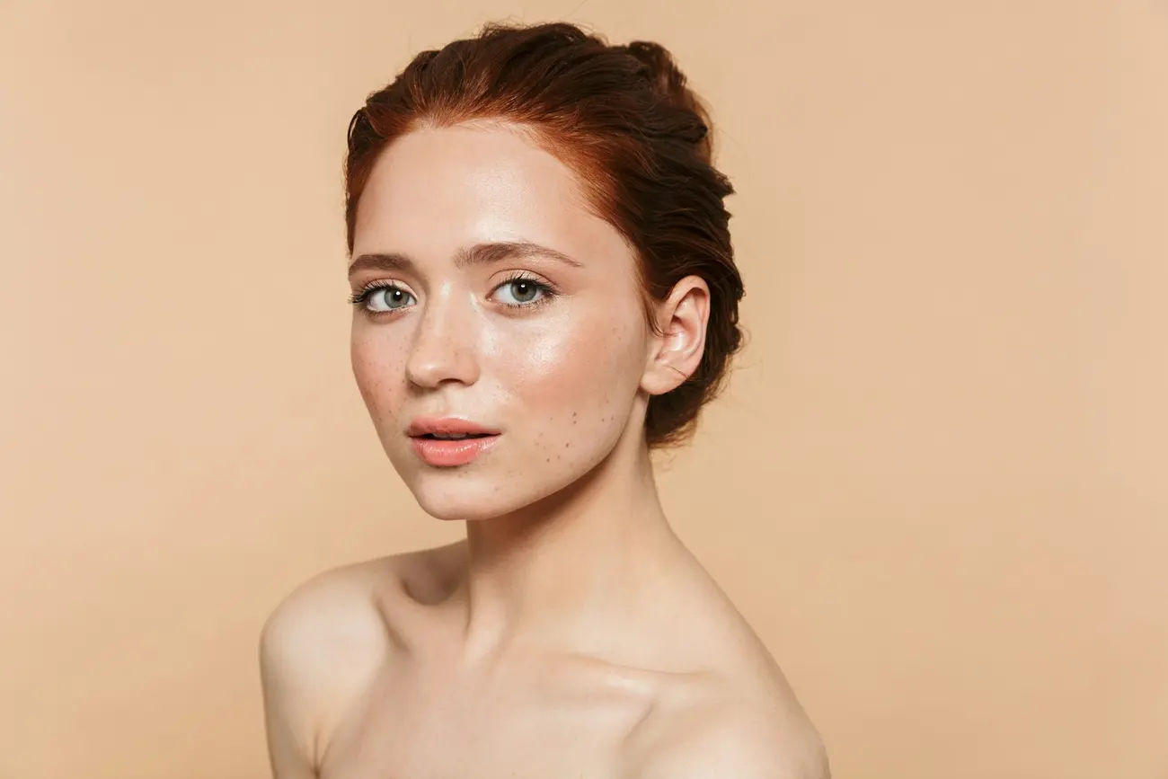 A studio portrait of a young woman with strawberry-red hair pinned up, bare shoulders