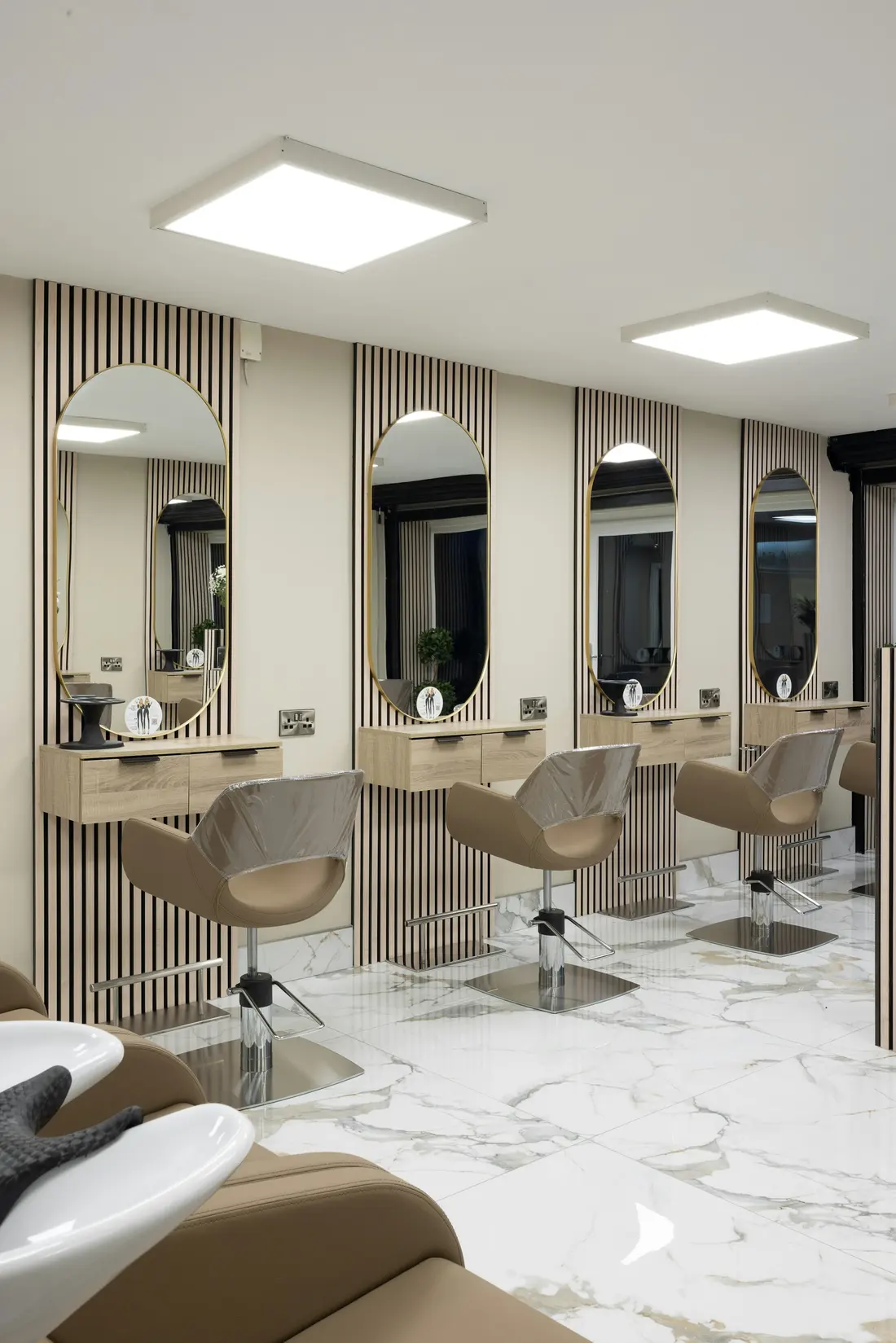 The salon floor: arched mirrors, cream chairs and pendant lights over a pale marble floor
