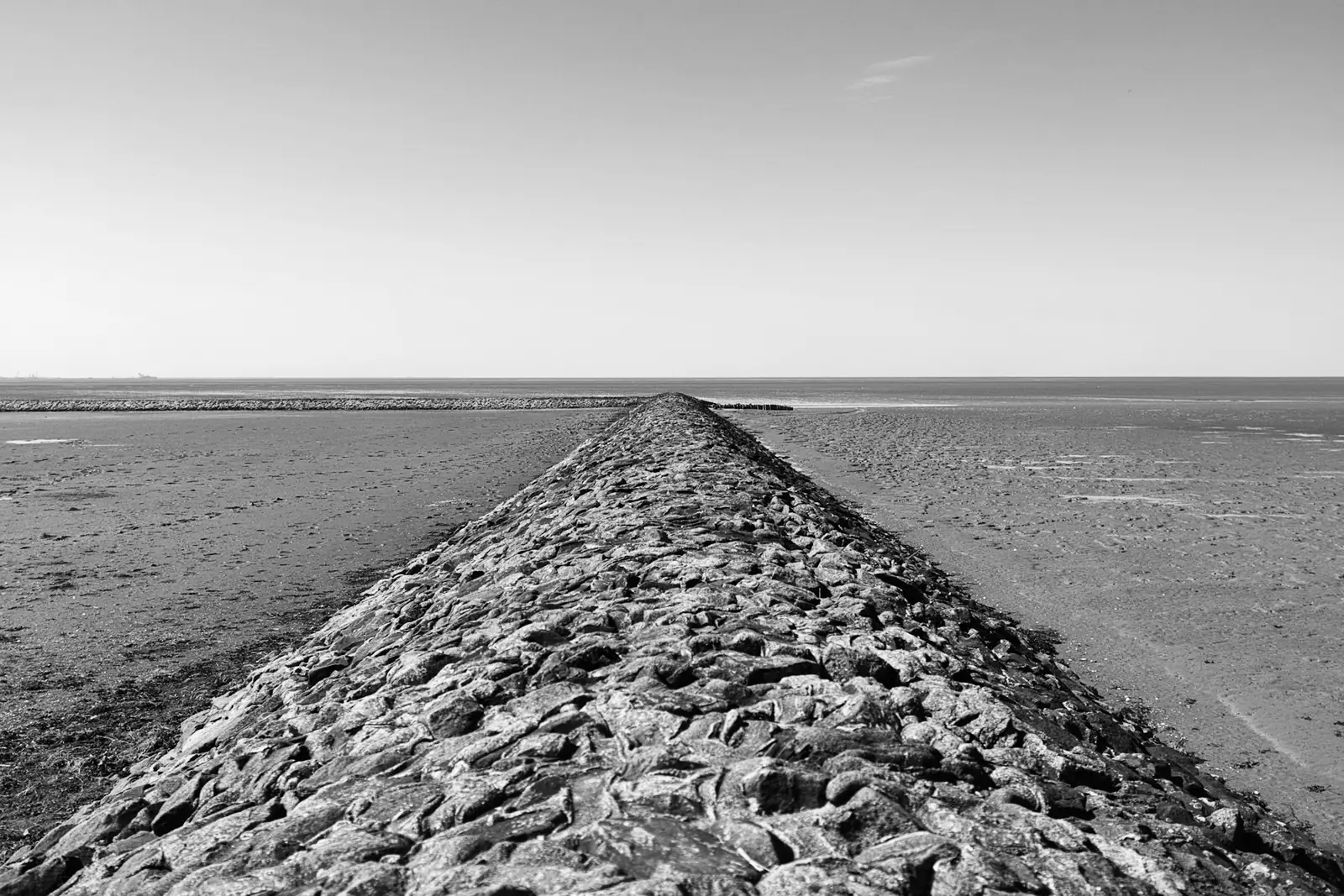 A stone breakwater running straight out across wet sand to the horizon at low tide
