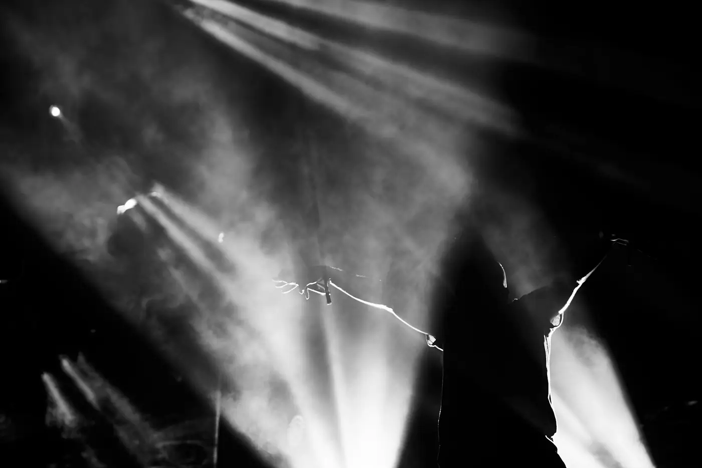 Beams of white stage light cutting through haze over raised hands