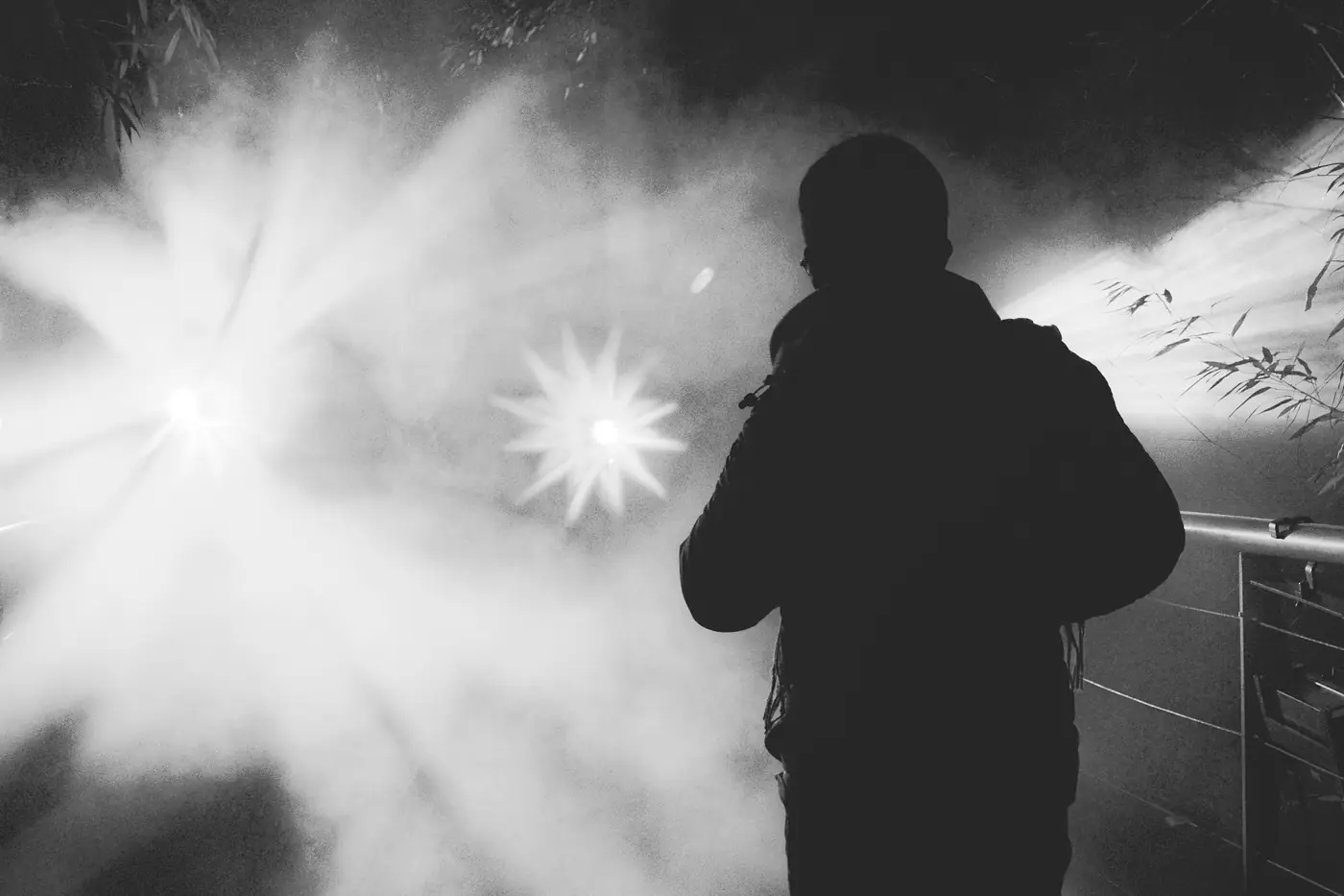 A hooded figure in silhouette against a burst of stage light