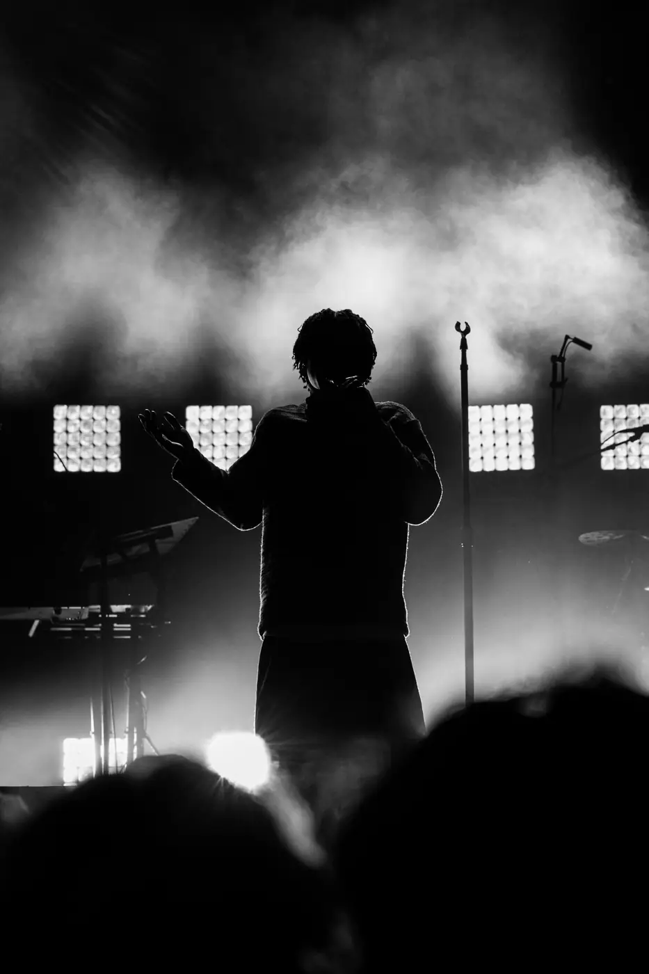 A performer with arms raised behind a row of lights, seen over the heads of the crowd