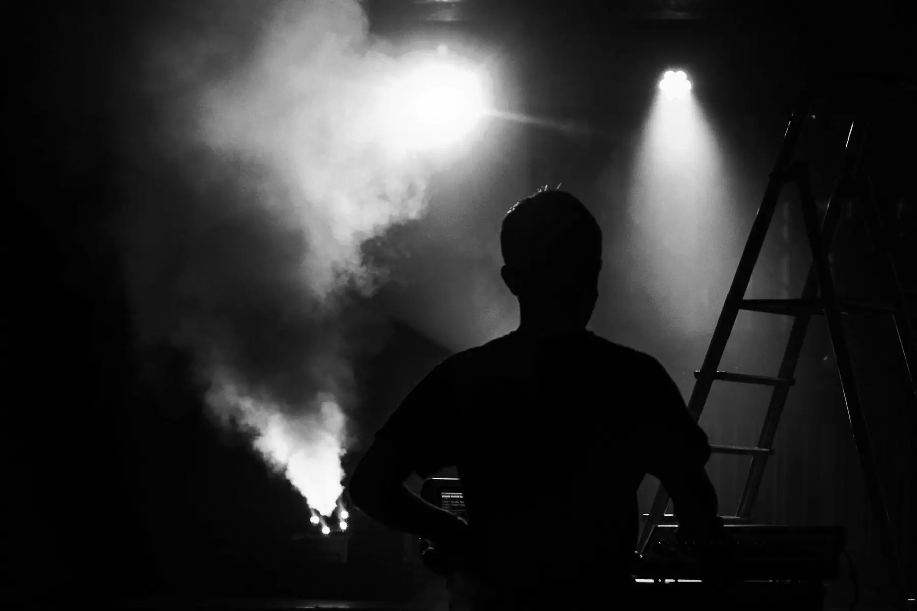A performer in silhouette against stage smoke and a single spotlight