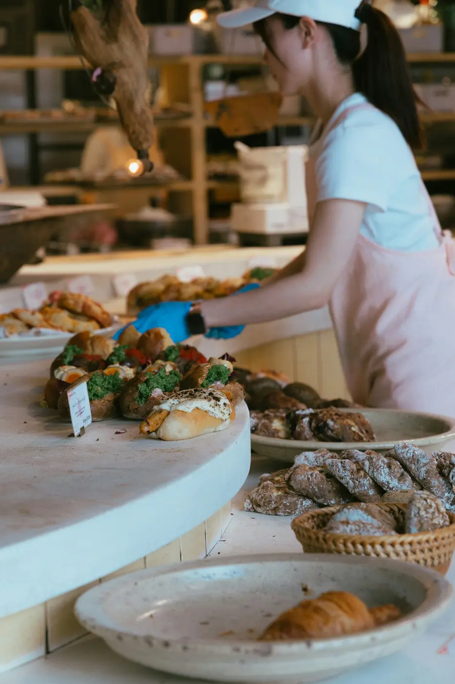 A baker in an apron arranging pastries on a wooden bakery counter