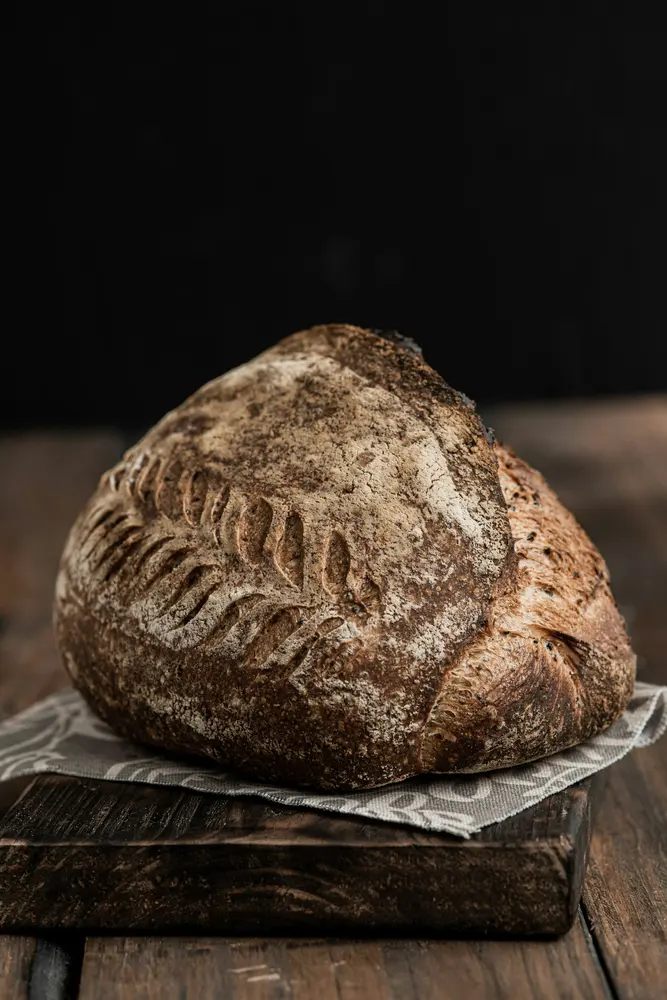 A dark-baked round sourdough loaf with scored crust on a wooden board