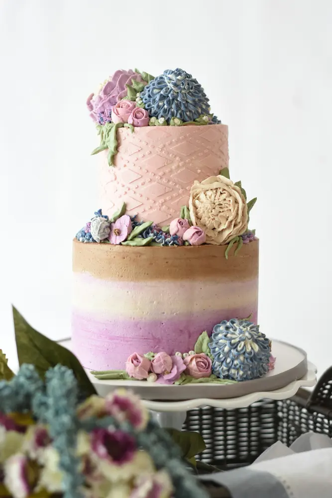 A two-tier ombré cake in pink and lilac with piped hydrangeas and succulents