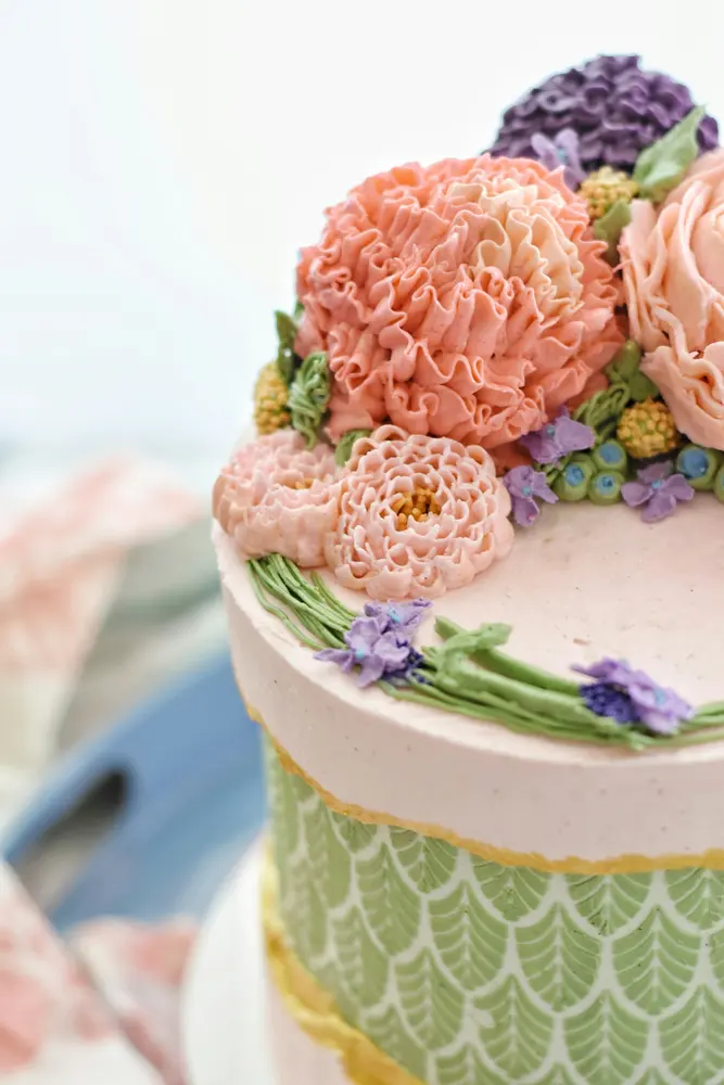 A single-tier cake crowned with piped buttercream peonies in coral, violet and pink
