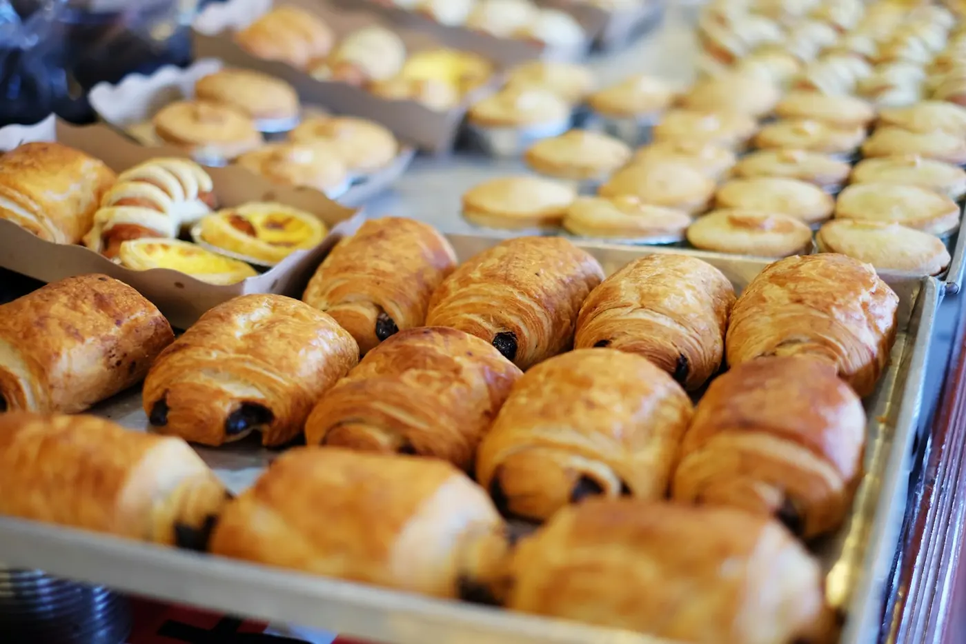 Trays of pain au chocolat and custard buns cooling on a bakery bench