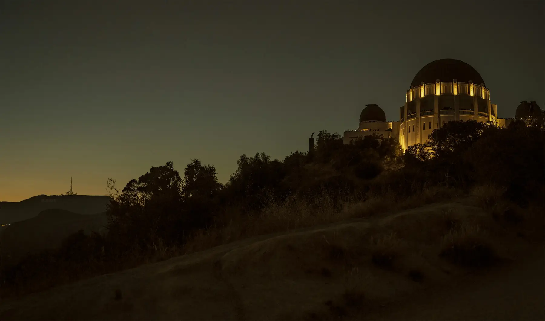 An observatory dome lit warm yellow on a dark hillside at dusk
