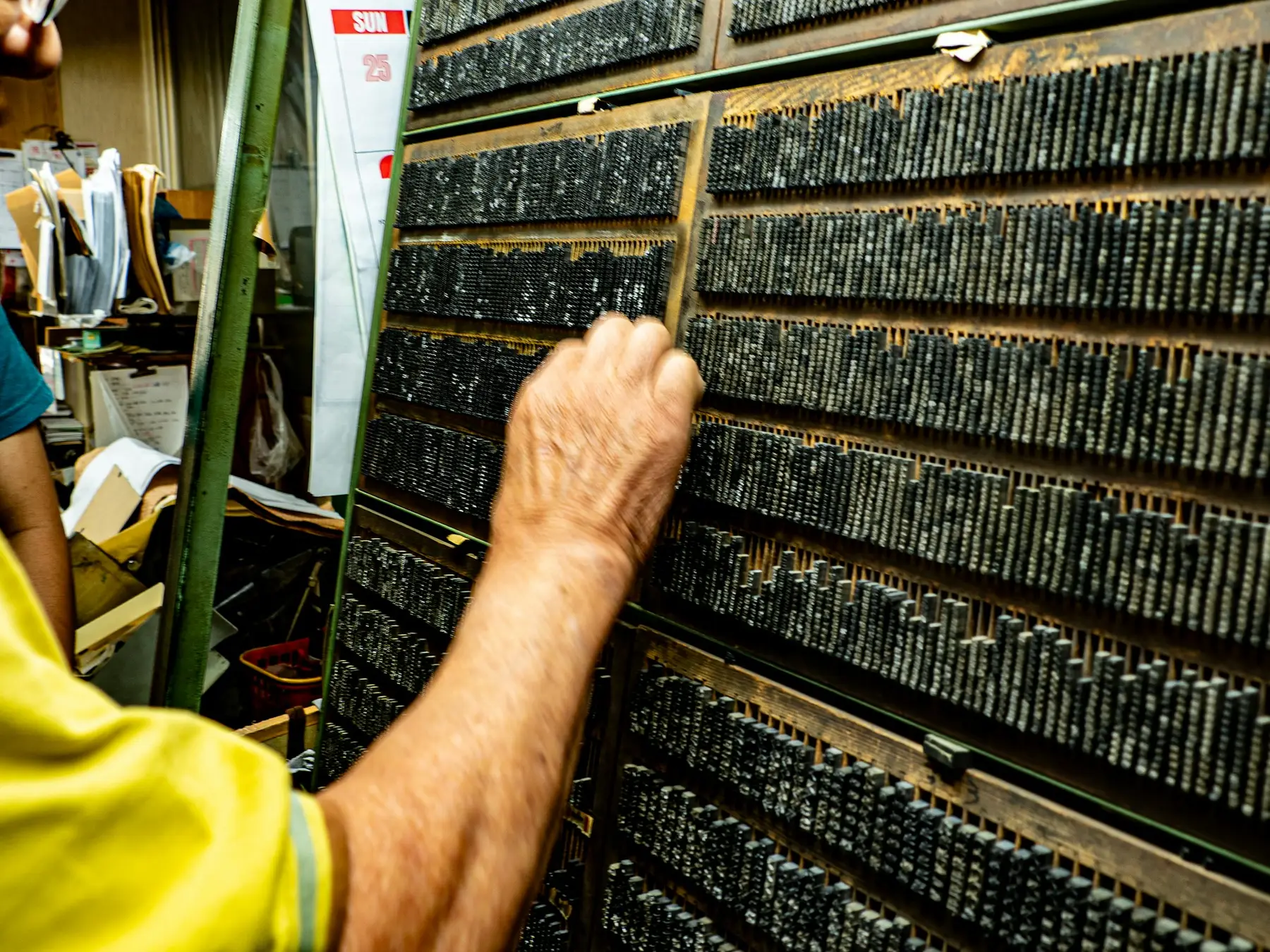 A hand choosing a piece of metal type from a tall wooden type case