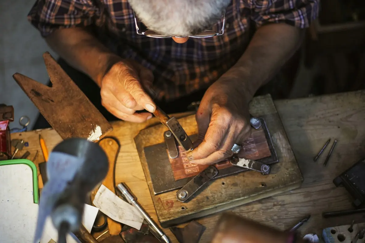 A goldsmith's hands piercing sheet metal with a fine saw at a wooden bench pin