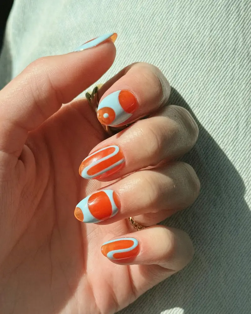 Short oval nails painted with orange and pale blue abstract swirls
