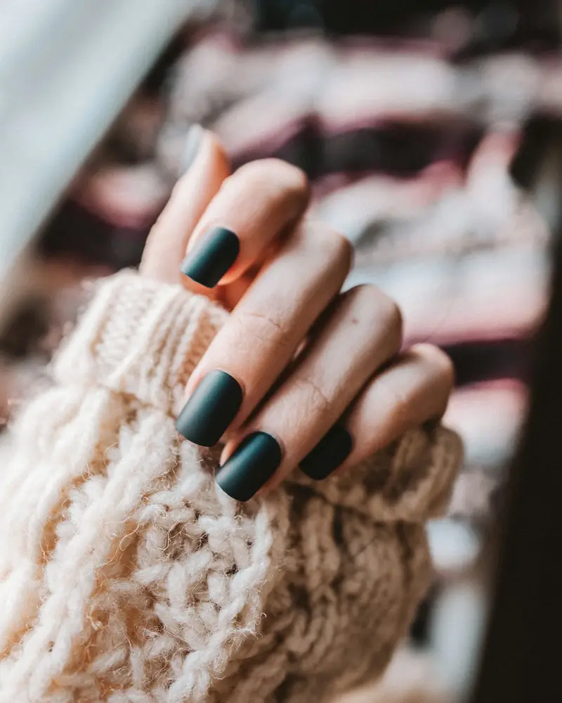 Short round nails in deep forest green against a cream knit sleeve
