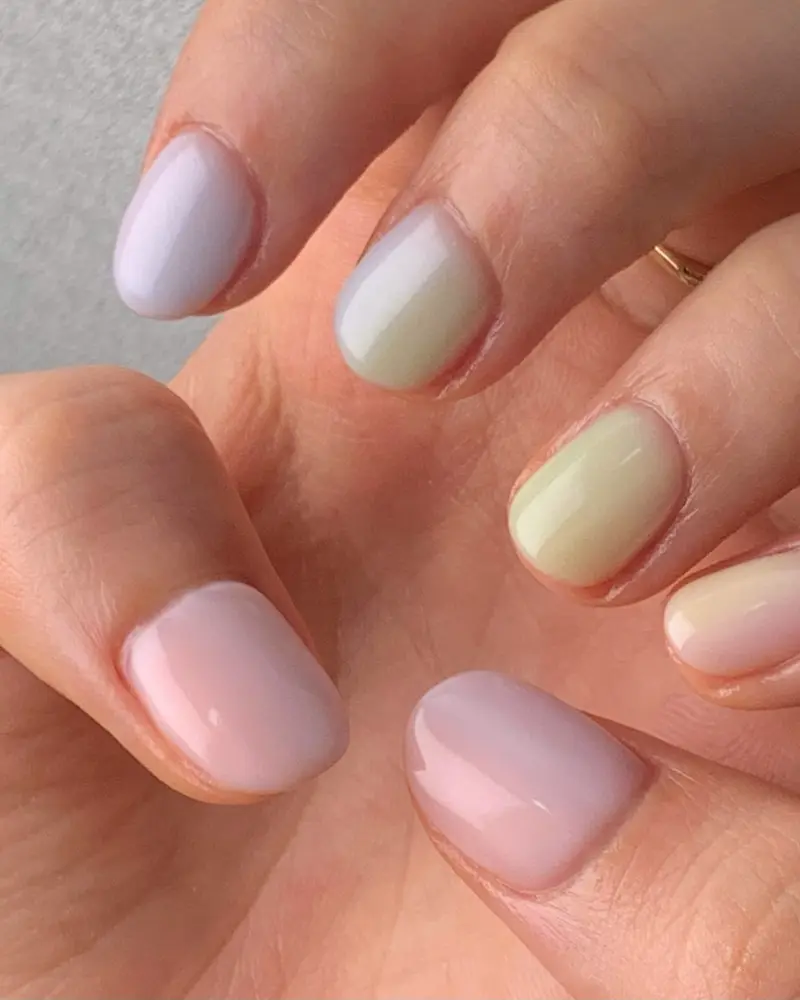 Short round nails, each a different pastel: lilac, sage, cream and pink