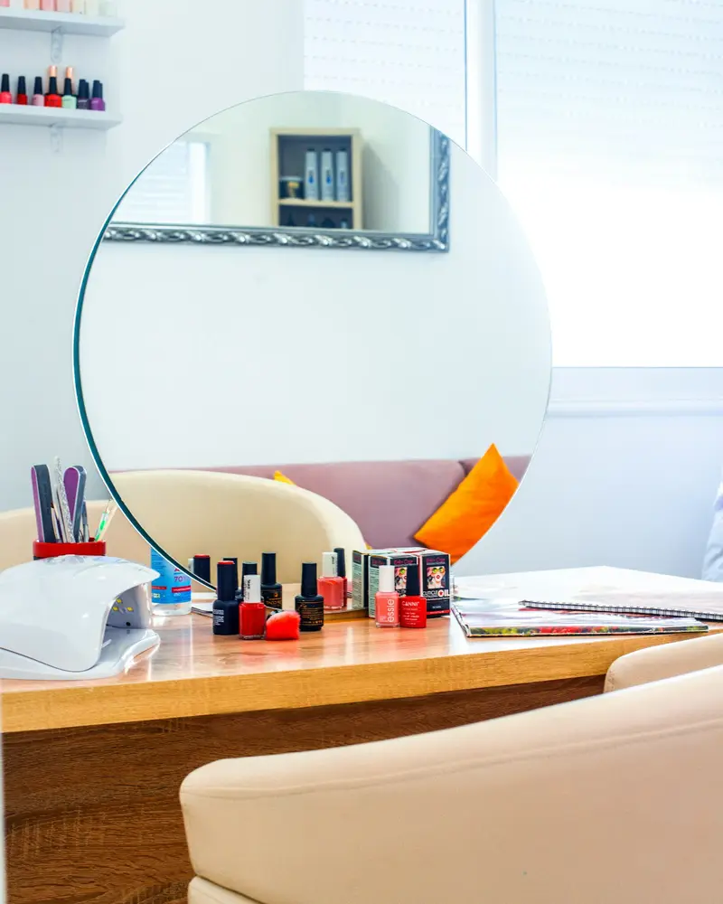 A tidy nail station with a round mirror, a lamp and a row of polishes
