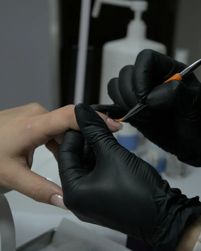 A nail artist in black gloves drawing a design with a fine brush