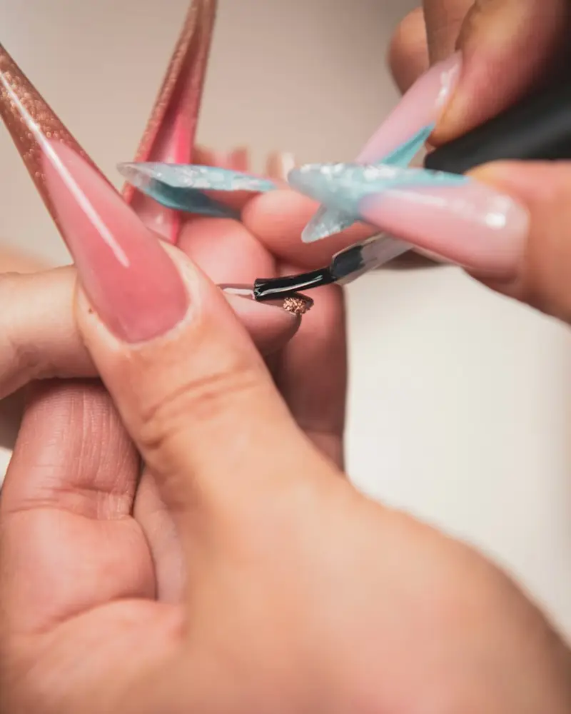 A manicurist painting a long pink stiletto extension with a fine brush