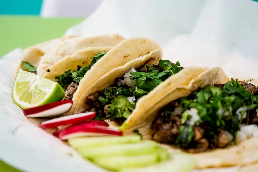 Street tacos with chopped meat, cilantro, radish and lime on a paper-lined tray