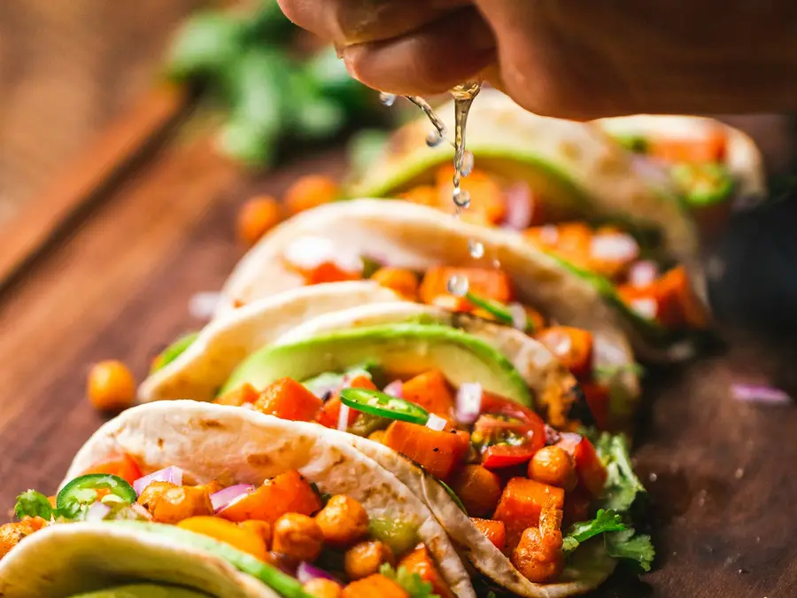Vegetable tacos topped with charred corn and peppers, a hand squeezing lime over them