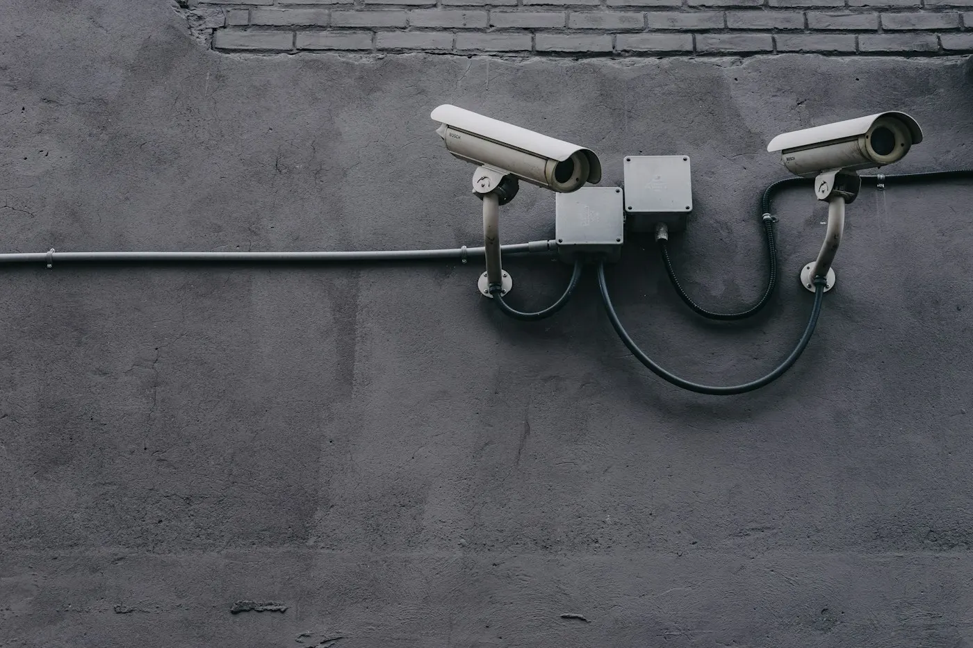 Two bullet cameras on a grey exterior wall with their cable in conduit