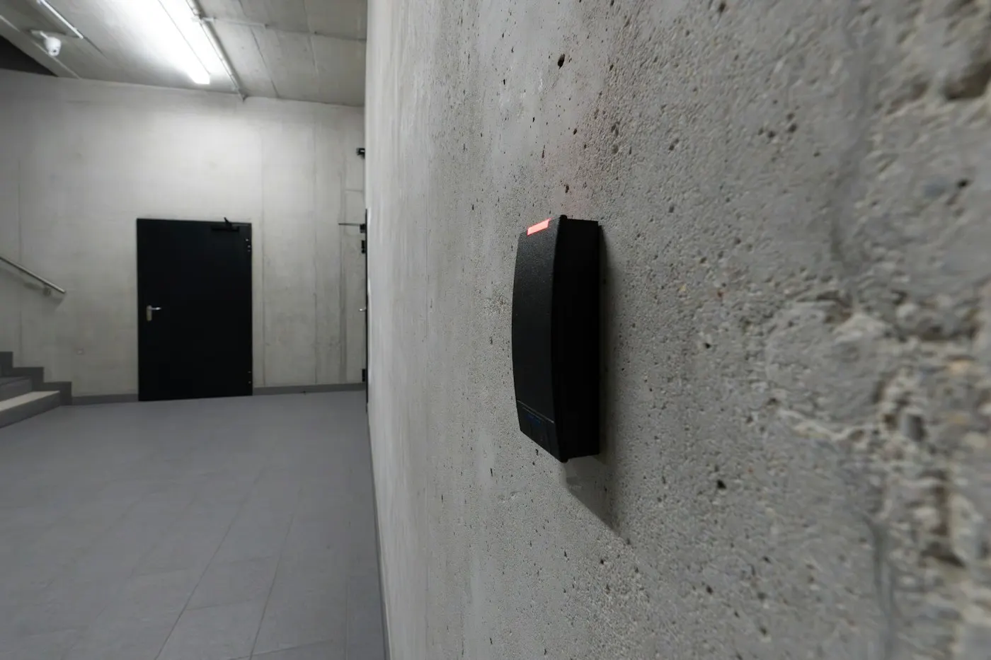 A black card reader on a concrete wall beside a stairwell door