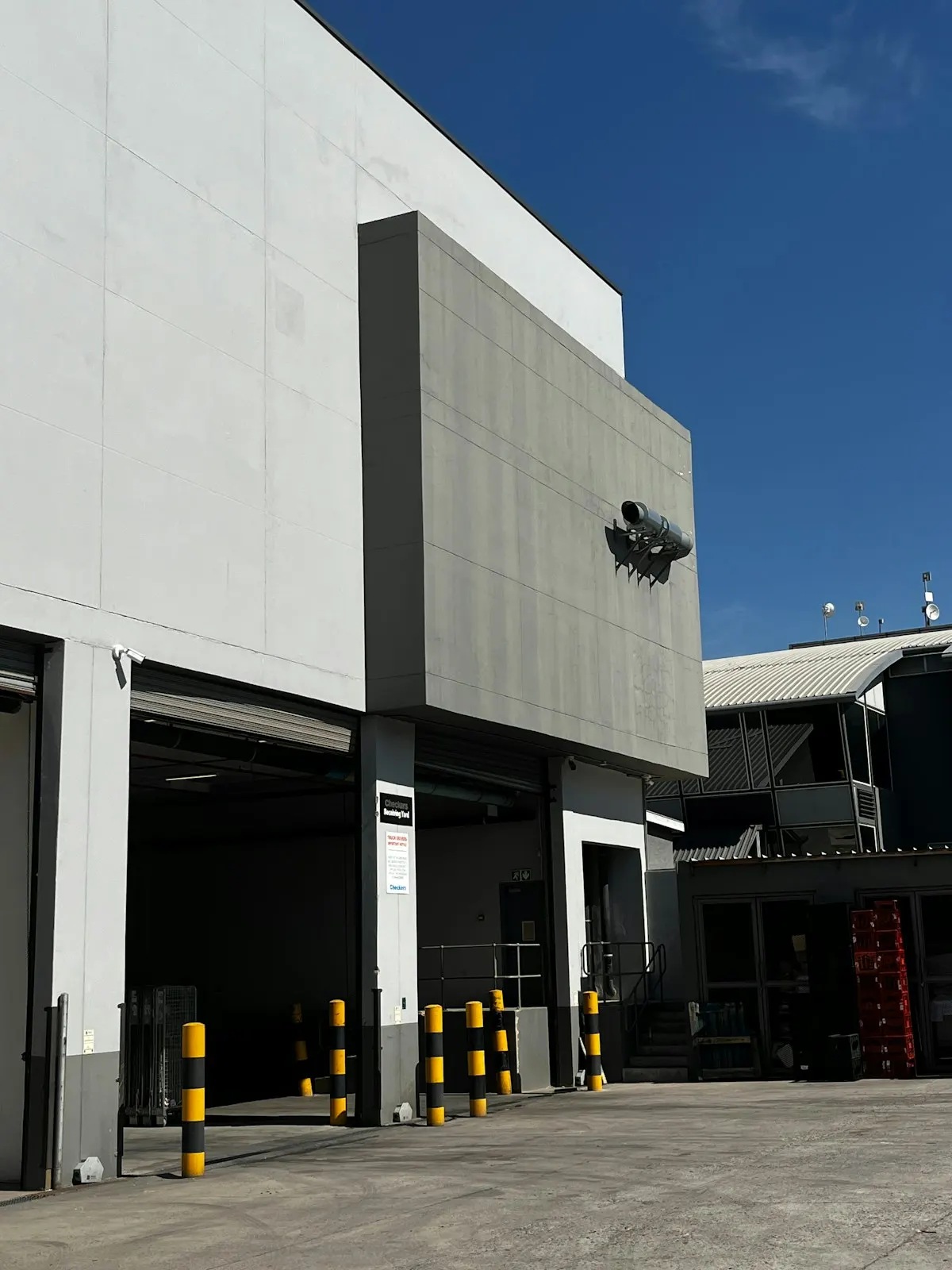 A warehouse with open loading docks and yellow bollards under a blue sky